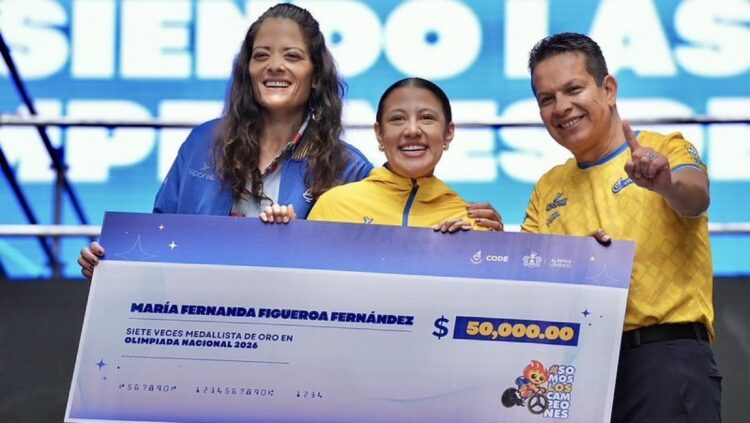 Maria Fernanda Figueroa Fernández sostiene un gran cheque simbólico junto a dos acompañantes, sonriente, en un evento de Olim.