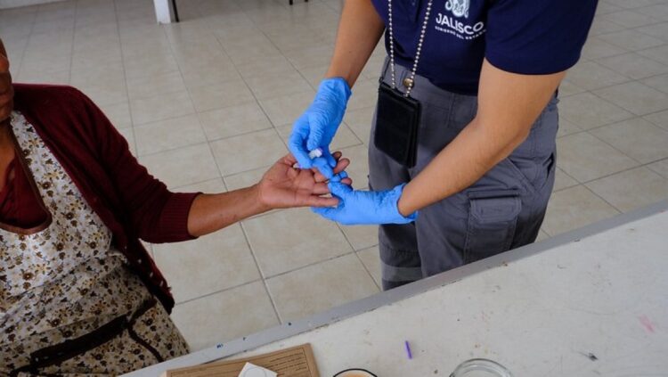 Una persona con guantes azules limpia el dedo de otra persona sentada, como parte de un procedimiento médico.