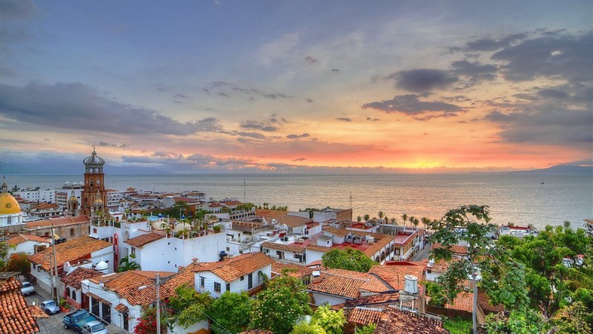 Vista de un pueblo costero con casas de techos rojos y el mar al fondo durante el atardecer.