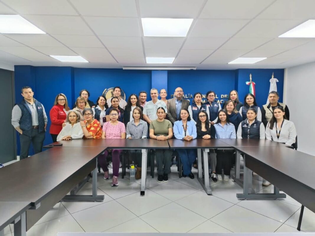 Un grupo de personas posa para una foto en una sala de reuniones con paredes azules y mesas en forma de U.