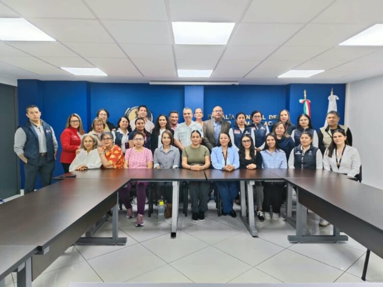 Un grupo de personas posa para una foto en una sala de reuniones con paredes azules y mesas en forma de U.