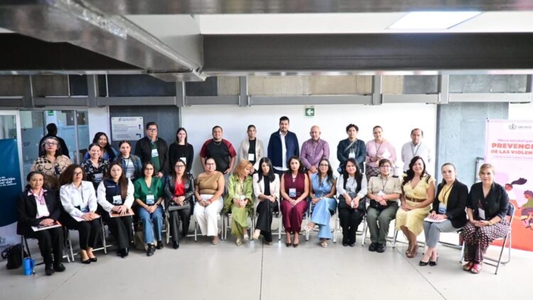 Un grupo de personas posa sentado y de pie en una sala de reuniones con carteles en el fondo.