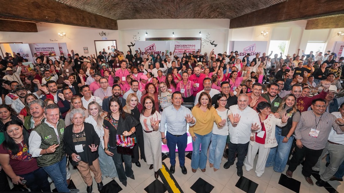 Un gran grupo de personas posa sonriente en el interior de un salón durante un evento comunitario.