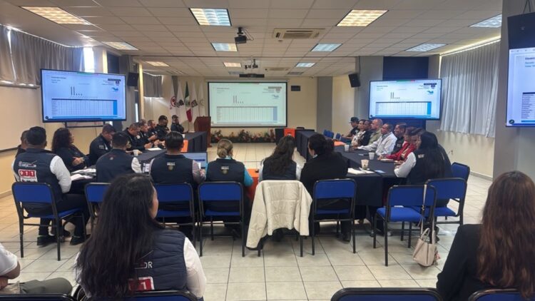 Un grupo de personas está sentado en una sala de conferencias viendo presentaciones en pantallas grandes.