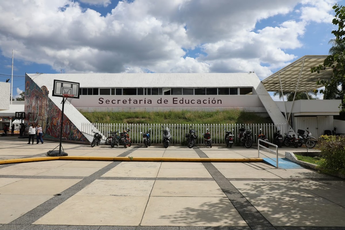 Fachada de la Secretaría de Educación en Morelia con motocicletas estacionadas y cielo parcialmente nublado