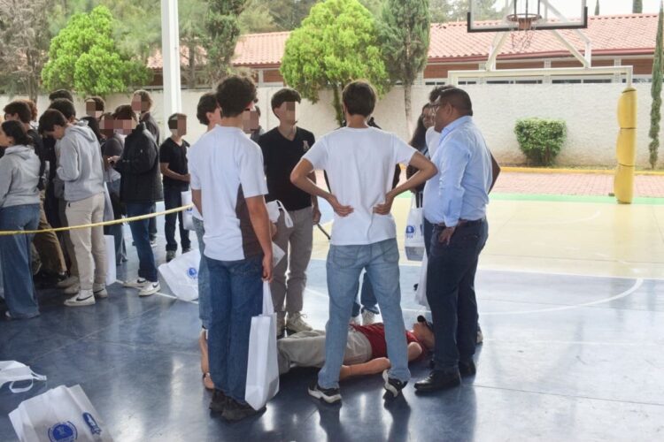 Un grupo de personas está reunido alrededor de un maniquí acostado en el suelo de una cancha cubierta.