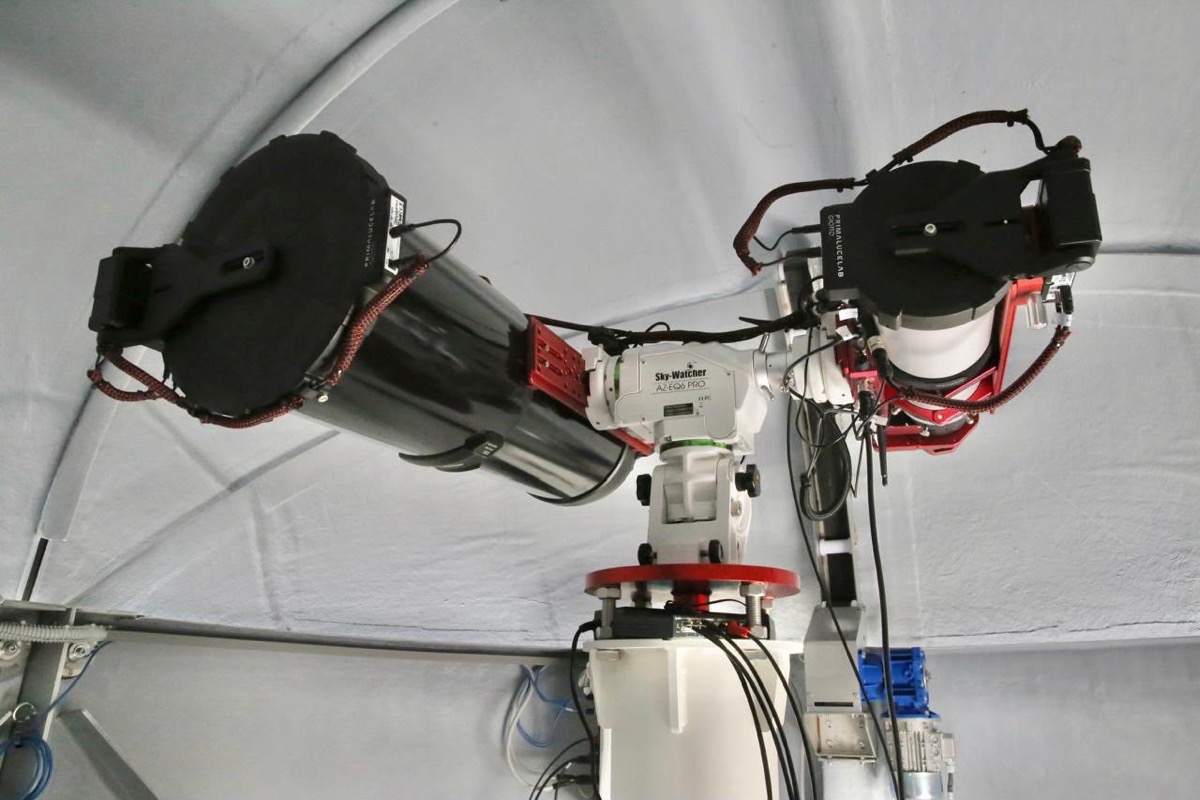 Dos telescopios montados en un soporte motorizado dentro de un observatorio cubierto.