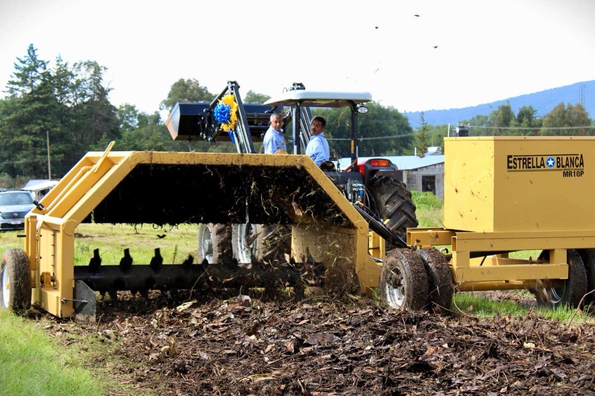 Un tractor arrastra una máquina amarilla que remueve y esparce hojas y tierra en un campo.