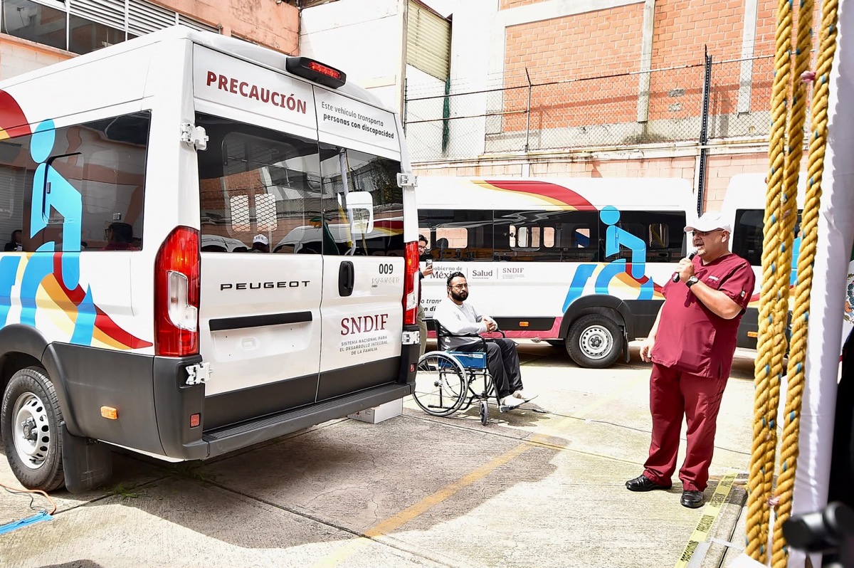 Un hombre en silla de ruedas y otro de pie junto a dos camionetas del SNDIF adaptadas para personas con discapacidad.