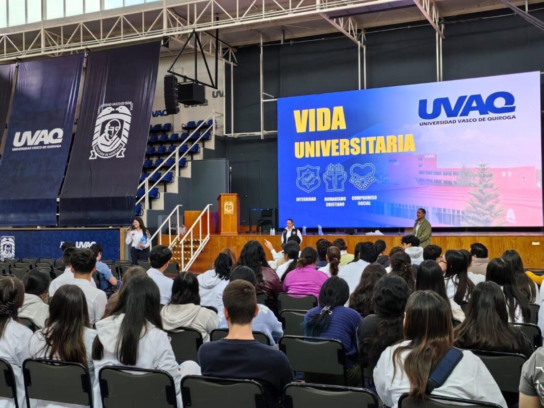 Un grupo de estudiantes está sentado en un auditorio mientras escuchan una presentación sobre vida universitaria en una pantalla grande.