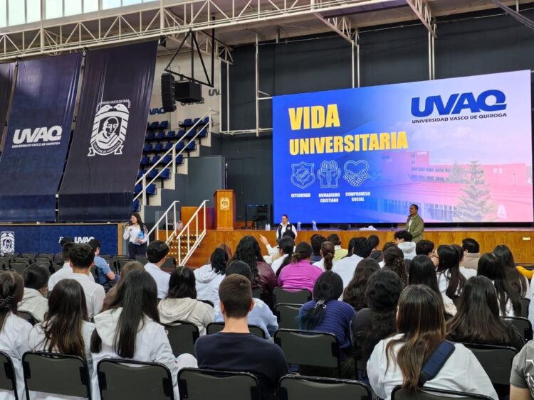 Un grupo de estudiantes está sentado en un auditorio mientras escuchan una presentación sobre vida universitaria en una pantalla grande.