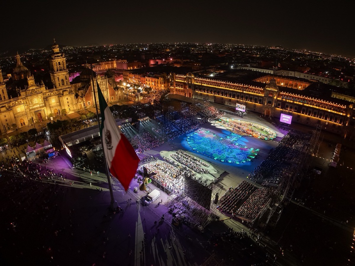 Espectáculo nocturno en el Zócalo de la Ciudad de México con bandera y público durante Fiesta de Culturas Comunitarias